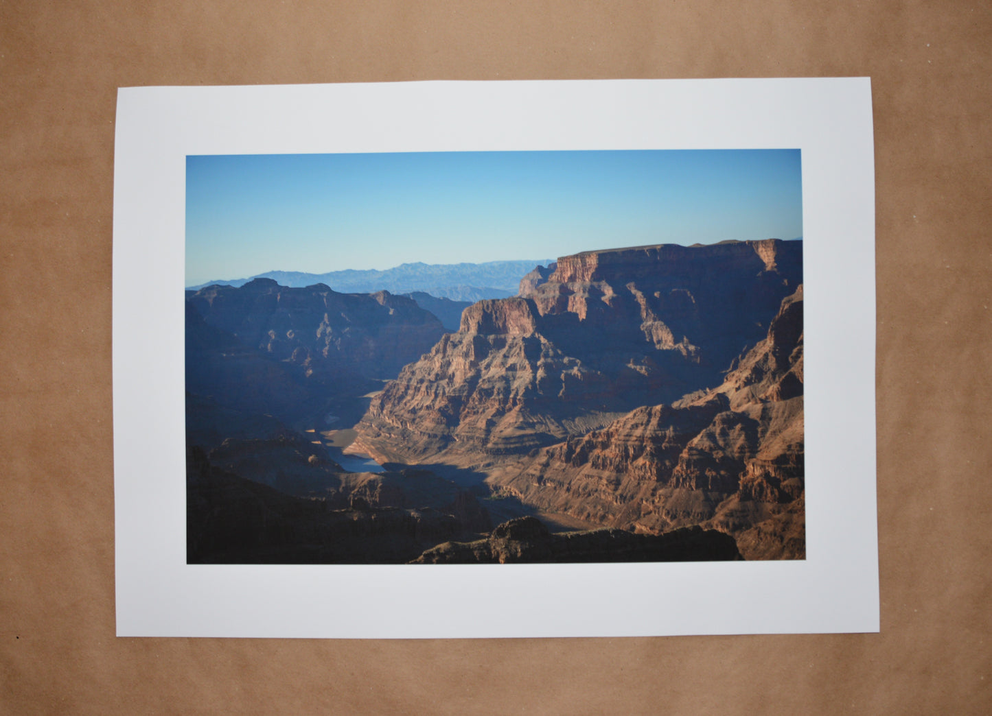 Grand Canyon shot with the river between the valleys of the canyons. Brown rugged mountains with striations alone the rocks. Blue skies.