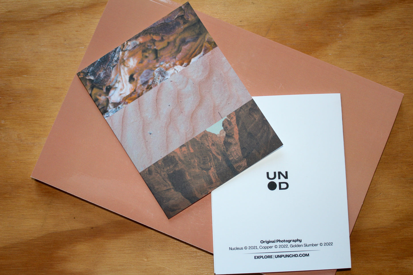 three original photographs that capture the natural beauty of tree bark, sands, and mountains. white card back with logo, photo names and years on an orange notebook background, on a wood background.