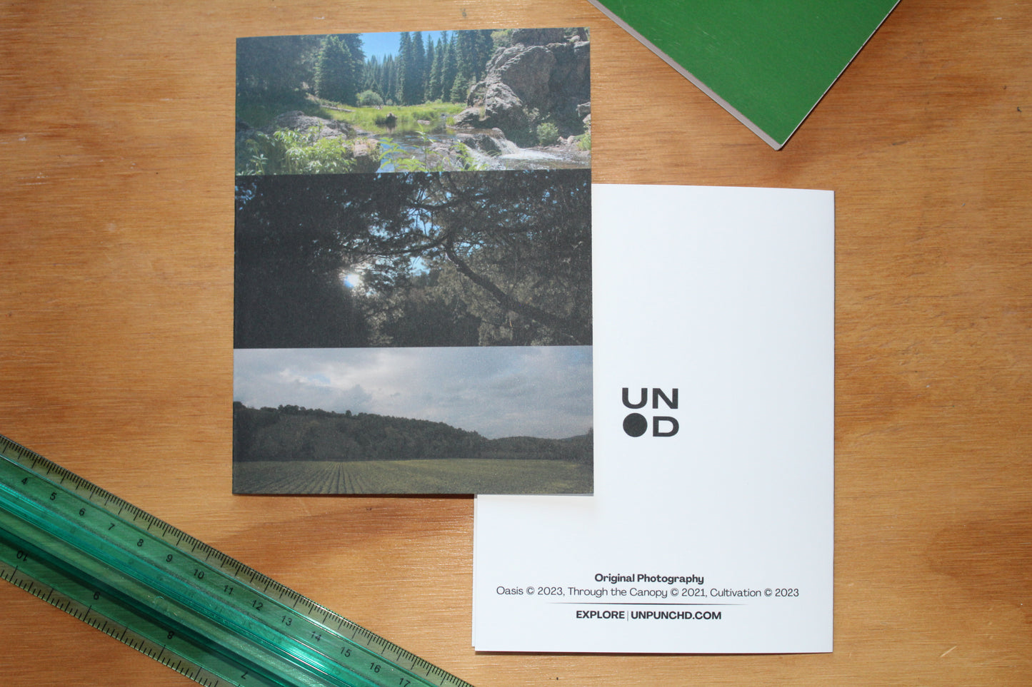 3 photos greenery, showcasing vibrant plants, leaves. wood background, green ruler and green notebook. white envelope and back of the card with the unpunchd logo and photography names and years produced with the website.