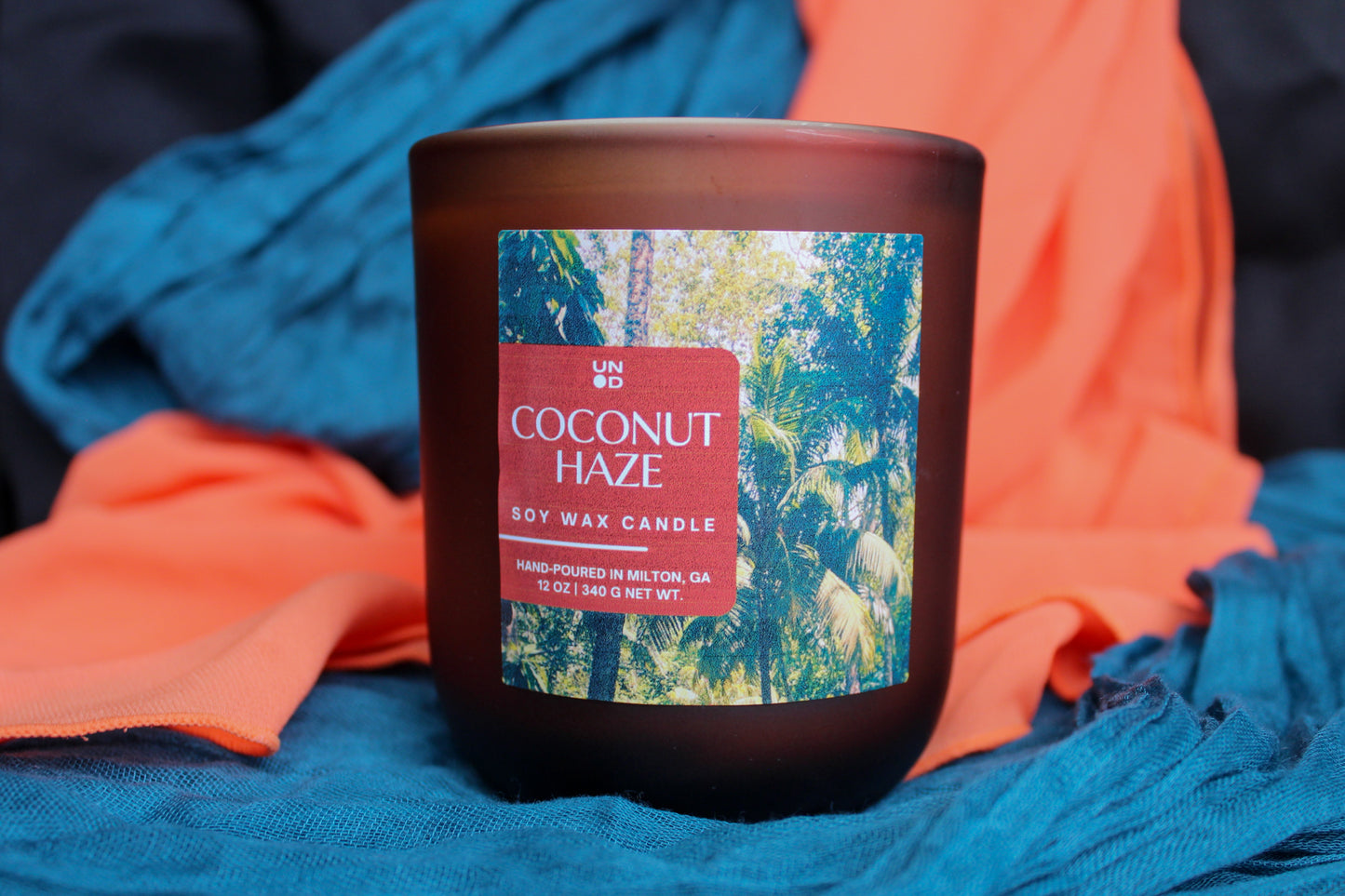 Coconut haze candle with colorful label on a blue and orange fabric background