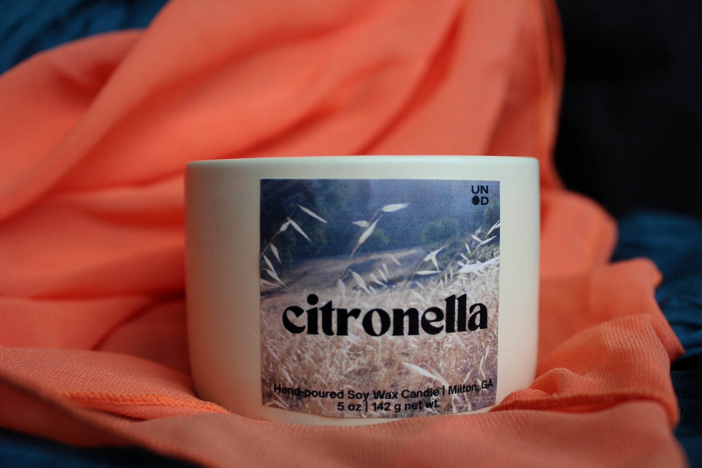 Buttercream candle labeled 'citronella' on an orange fabric background