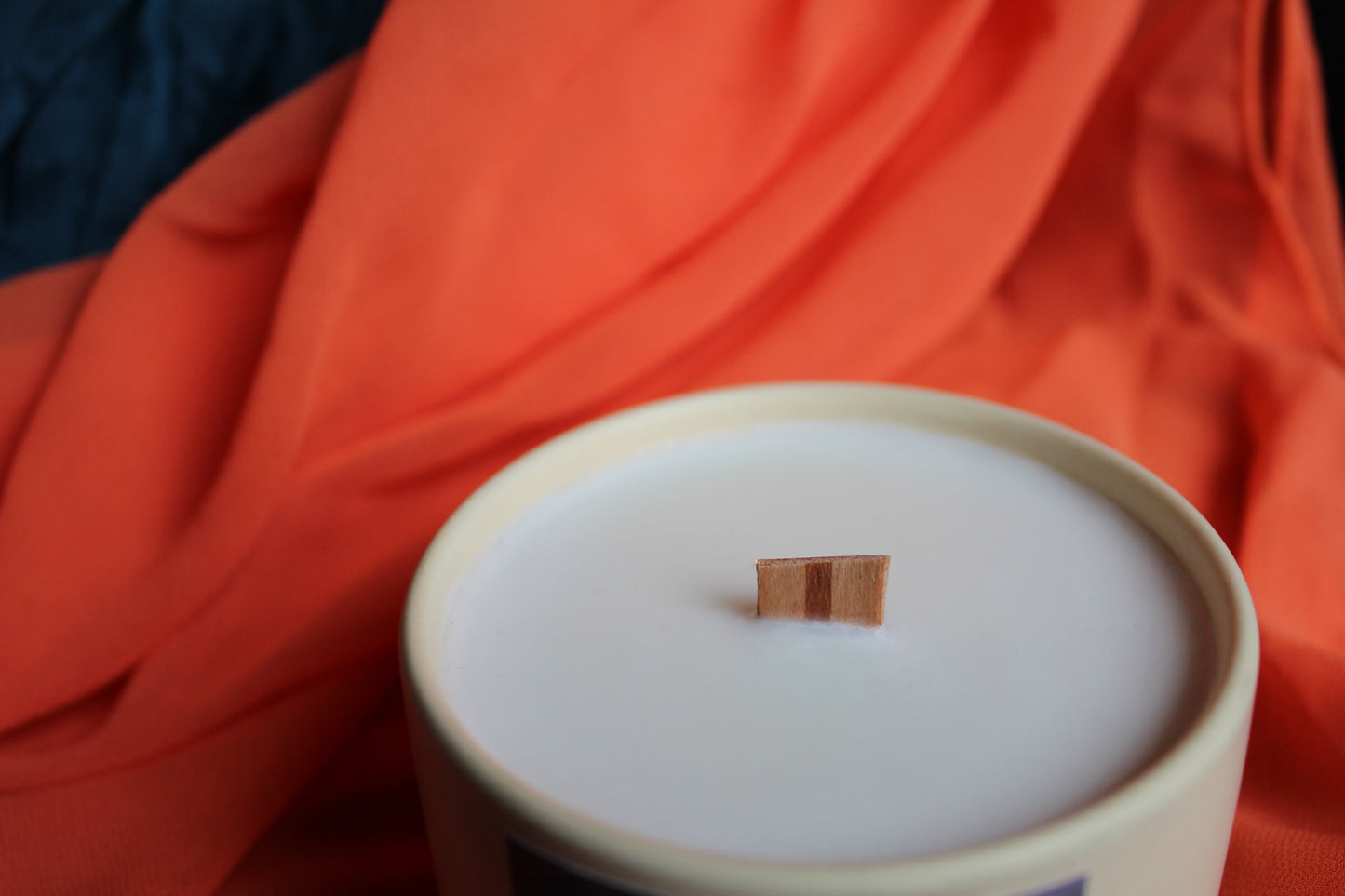Wooden wick on a white candle with an orange fabric background