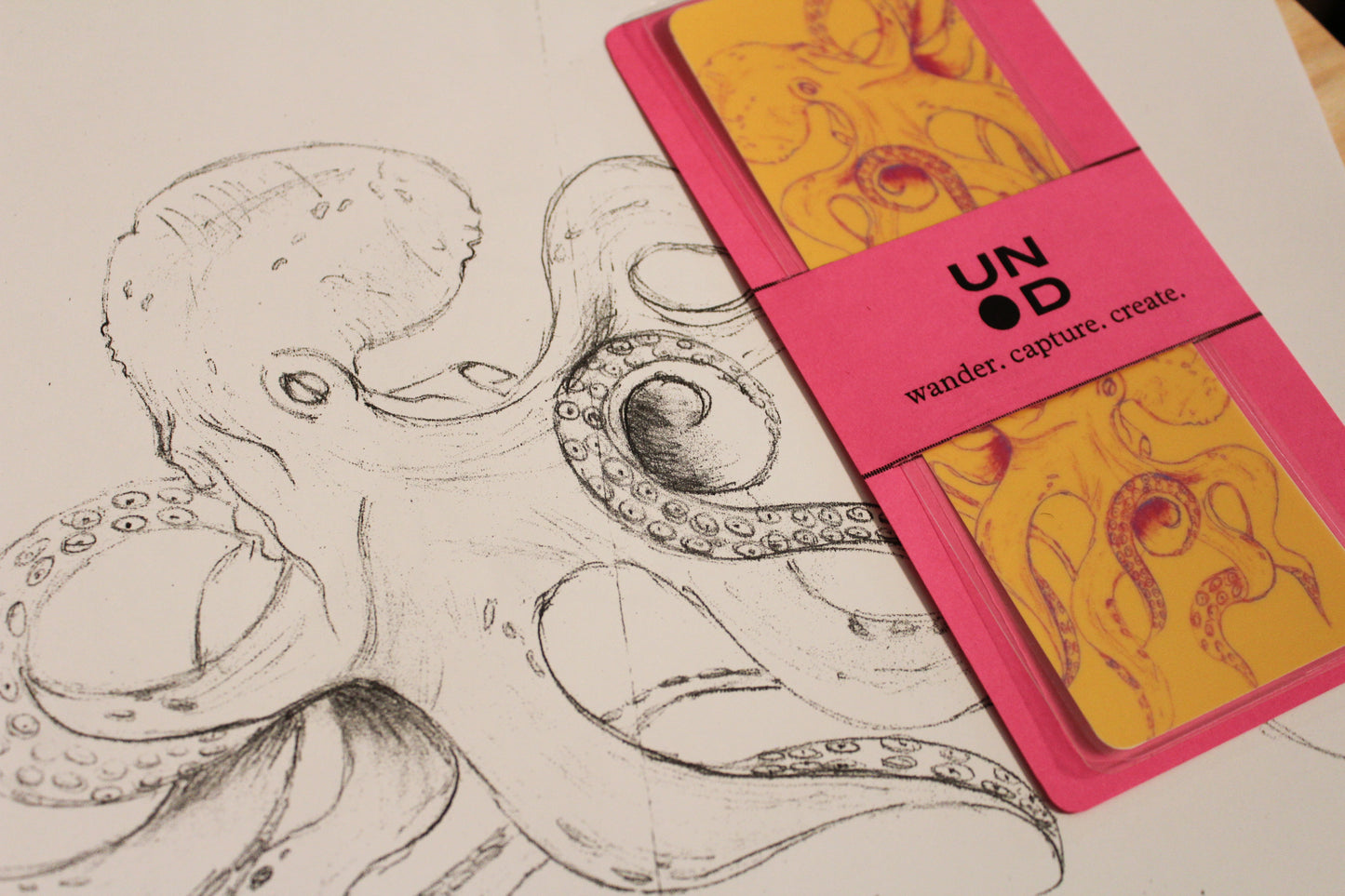 Pink bell band with yellow bookmark next to a black and white octopus illustration.