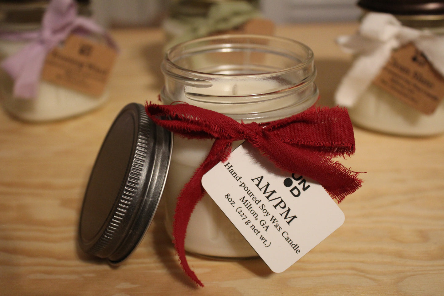 AM/PM candle with red tie and tag on wood surface with candles in the background