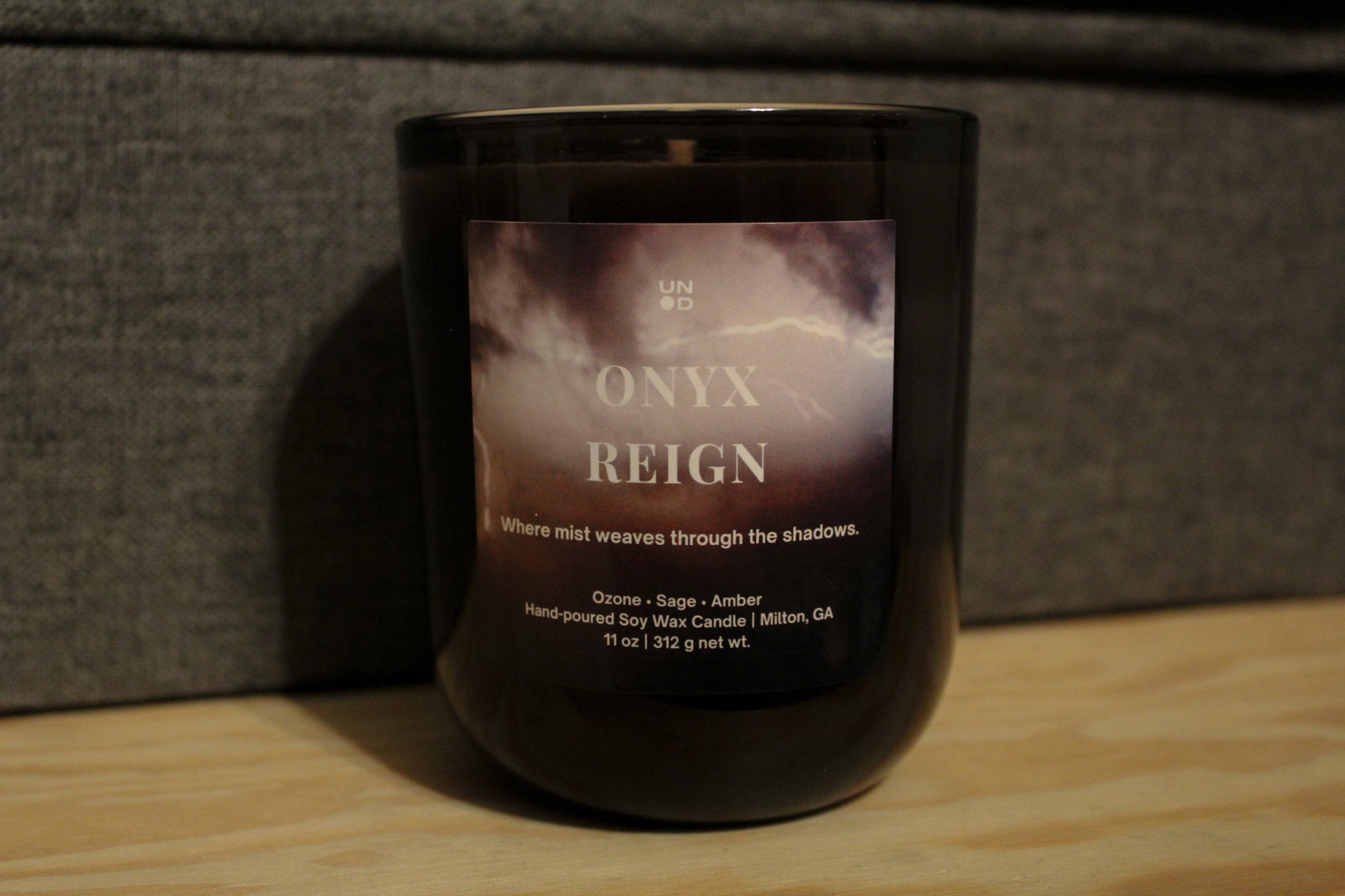 Onyx reign black candle, lightning strike label on textured grey background and wood base