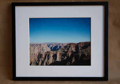 11x14 framed photo of the Grand Canyon with an ombre blue skyline. White matting with a black frame. 