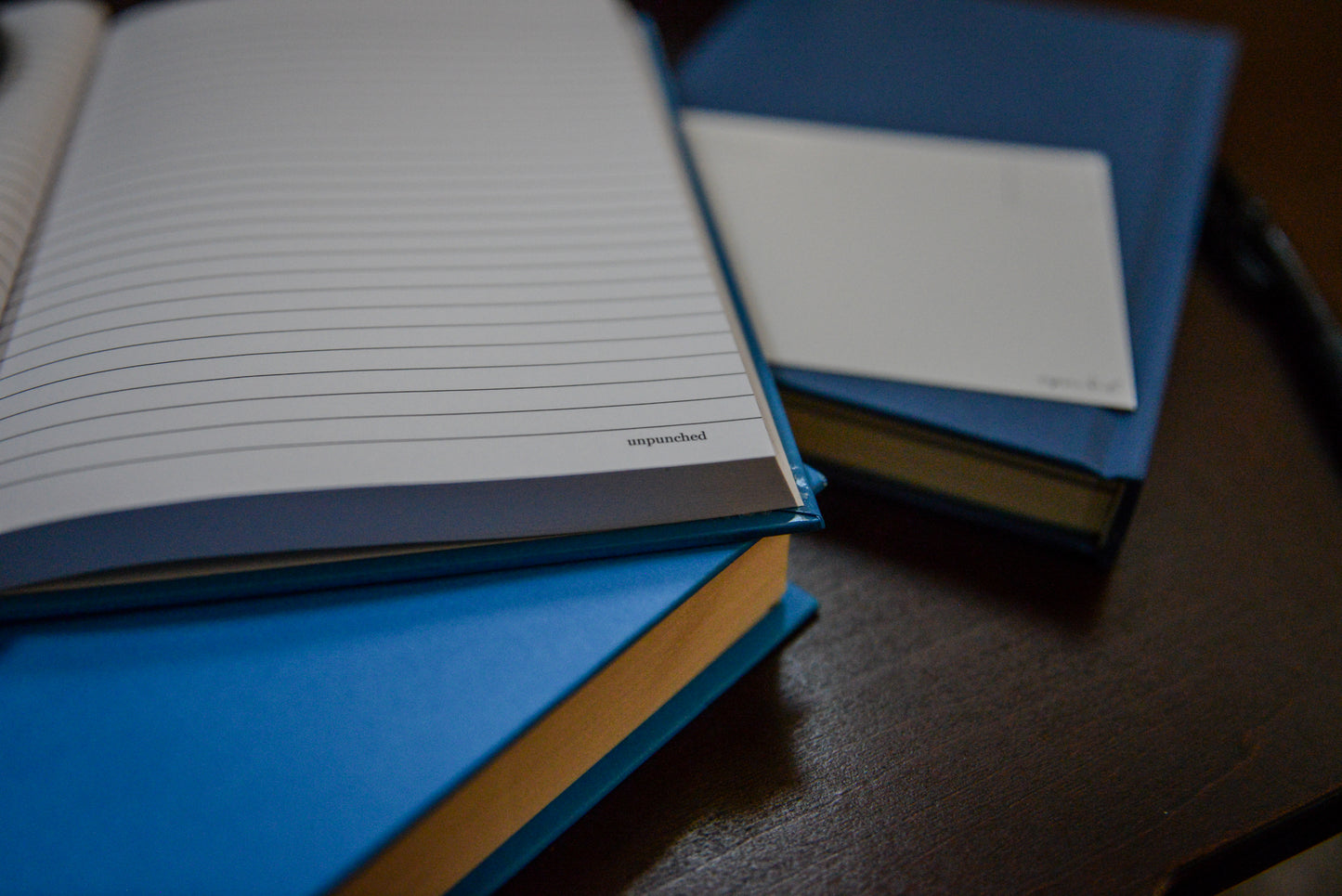 Unpunched notebook opened with lined rule, with unpunched in the right bottom corner of the pages. Notebook sitting upon blue books.