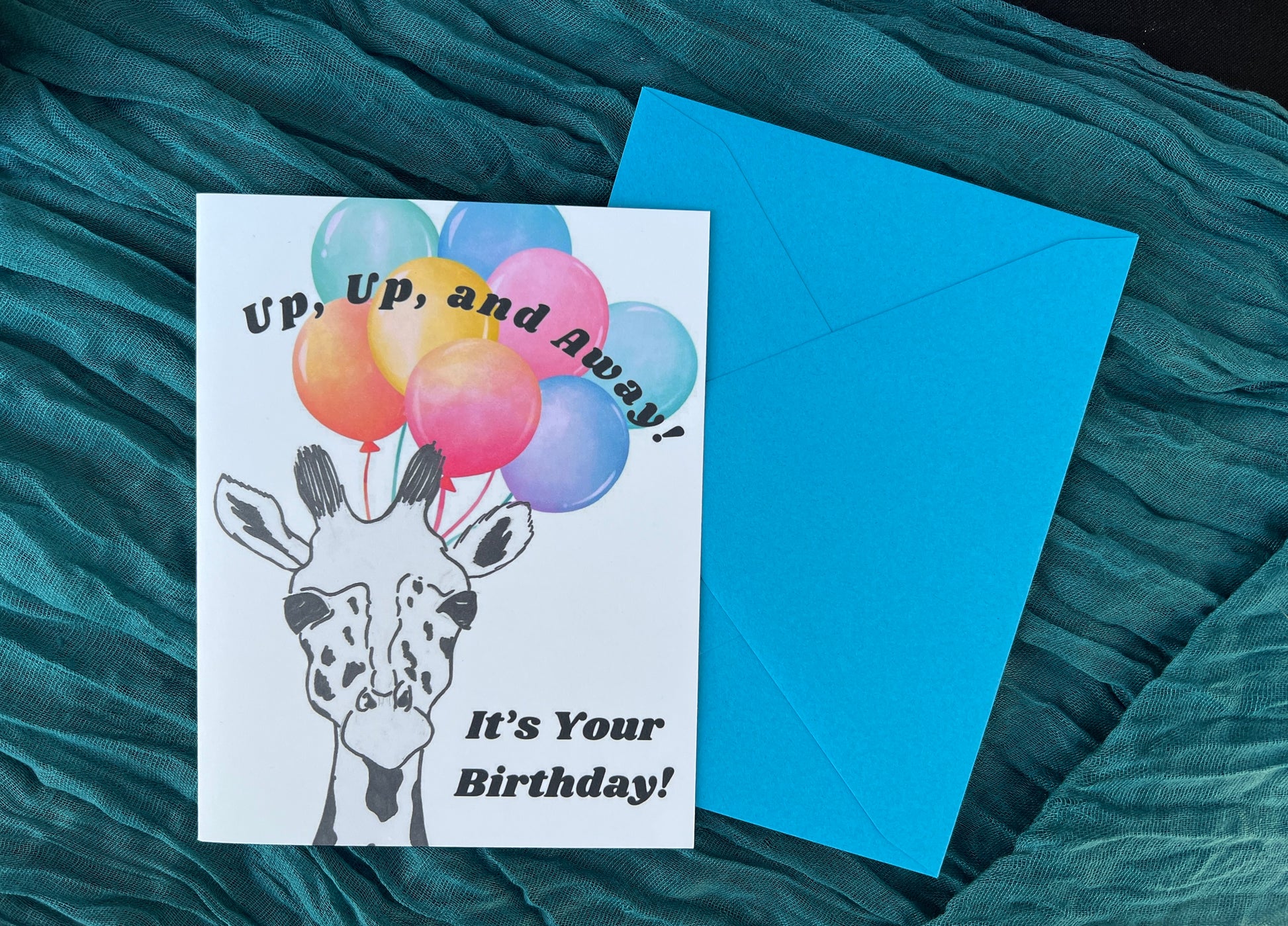 Greeting card with balloons and giraffe illustration on a teal fabric background