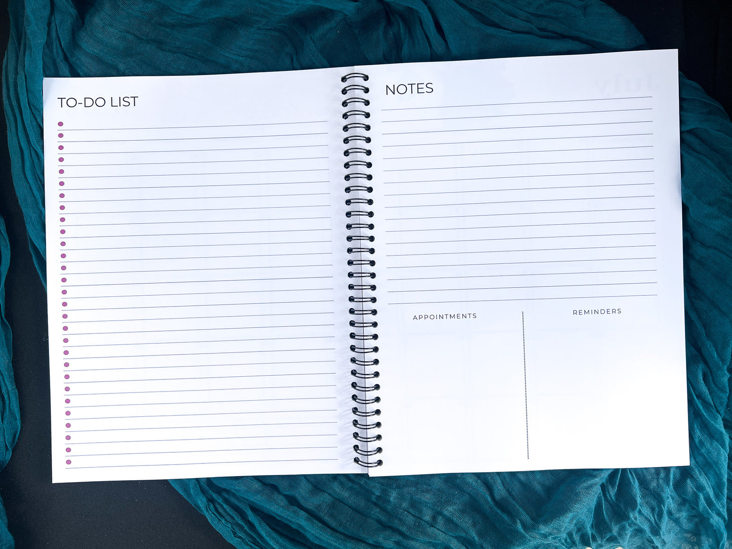 Open spiral-bound planner with to-do list, notes, appointments, and reminders sections on a teal fabric background.