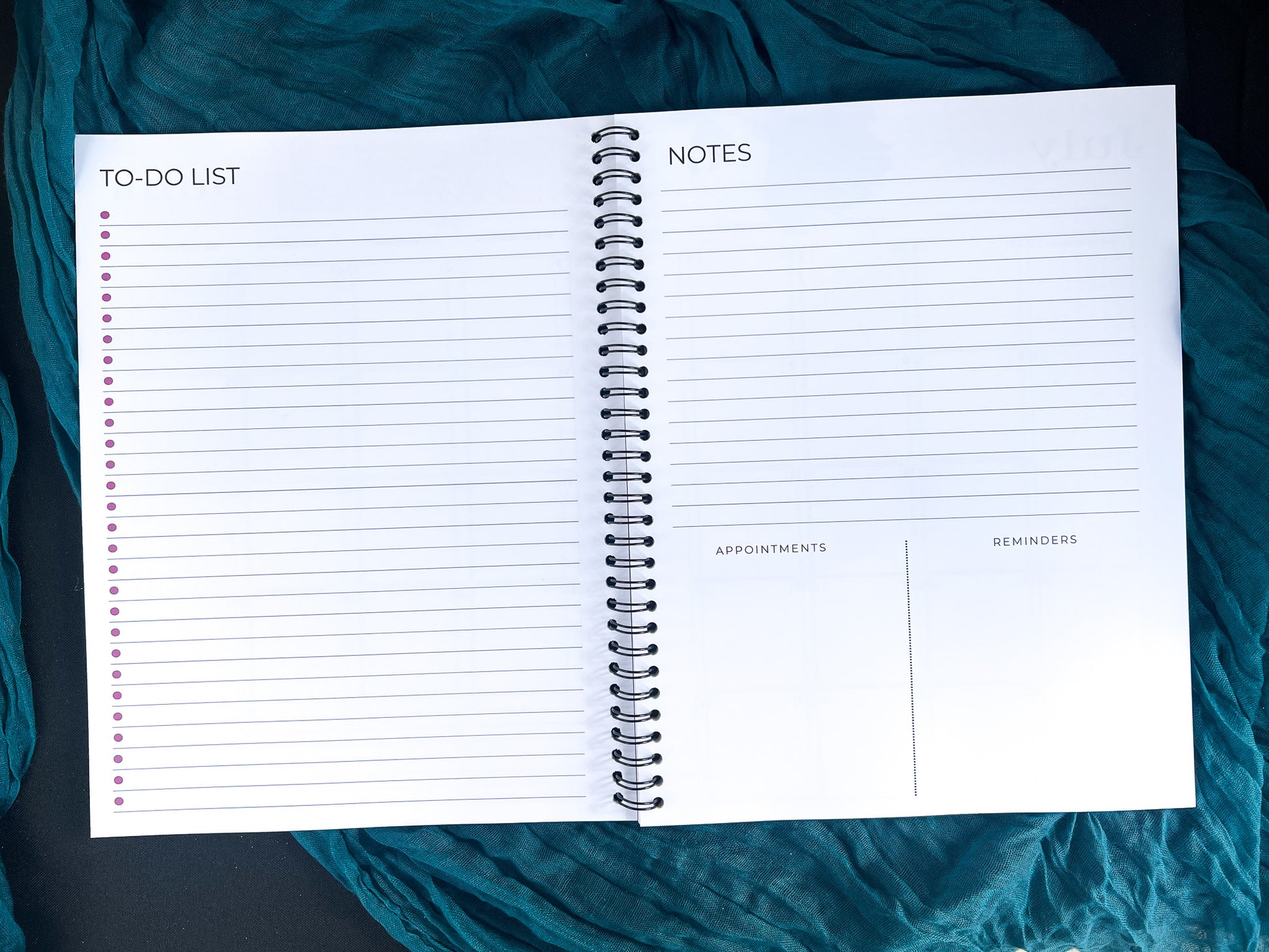 Open spiral-bound planner with to-do list, notes, appointments, and reminders sections on a teal fabric background.