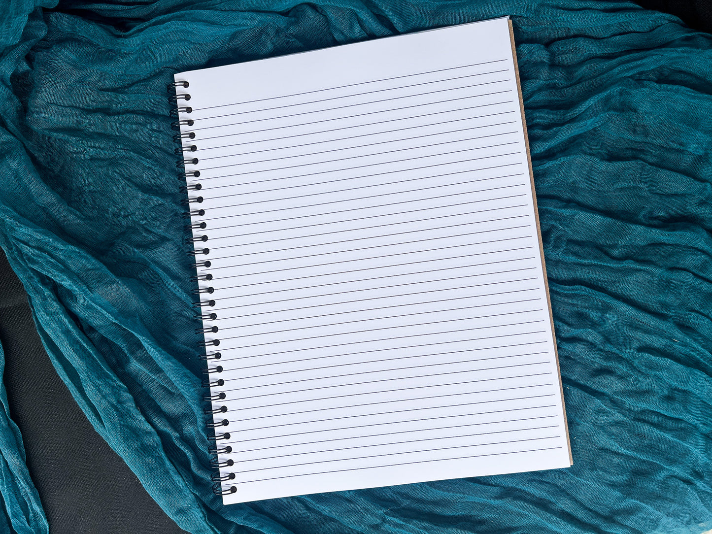 Blank notebook on a textured teal fabric background