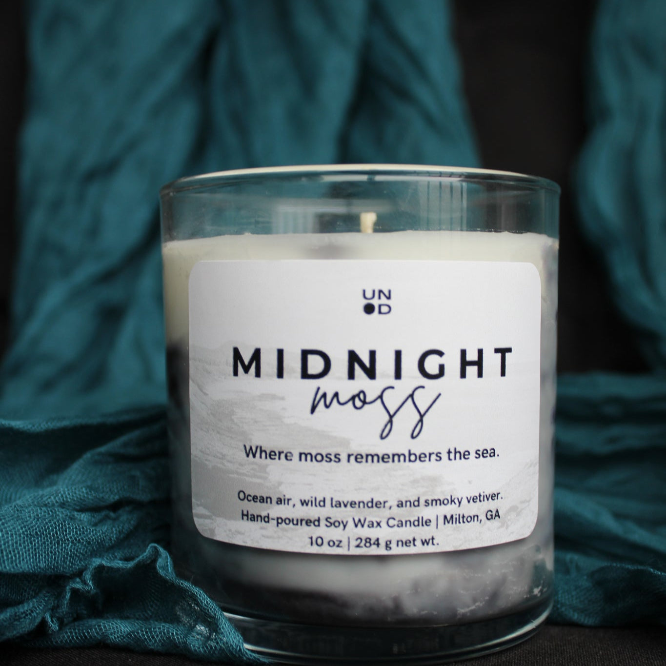 Candle labeled 'Midnight Moss' with a teal fabric background