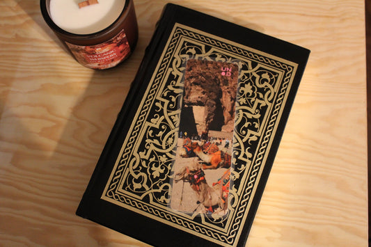 Decorative book with intricate design on a wooden surface next to a candle with camel bookmark on it