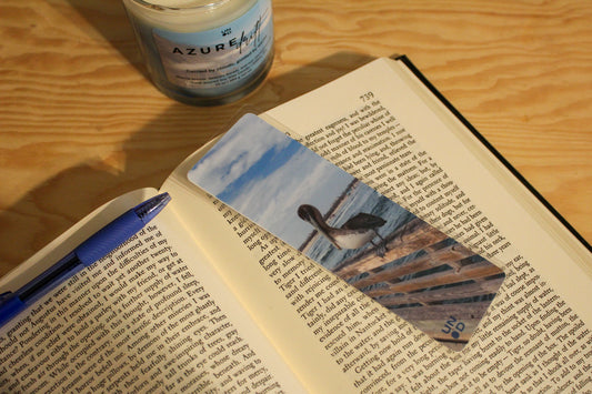 Open book with a bookmark featuring a pelican, pen, and jar on a wooden surface