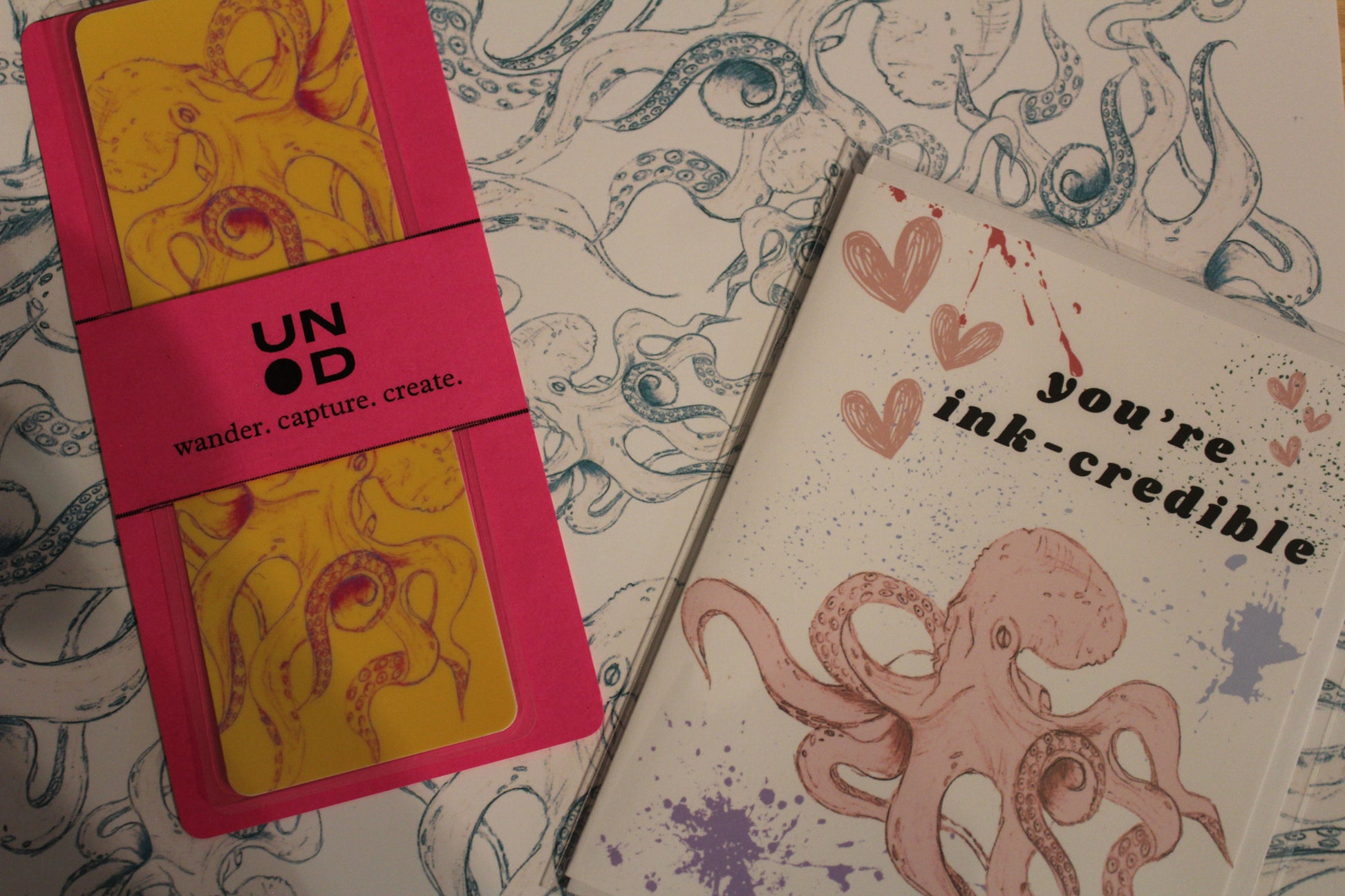 greeting card with 'you're ink-credible' text and octopus design on a notebook background and a pink book belly with yellow bookmark