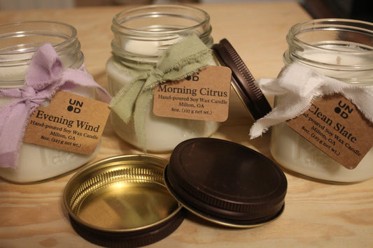 Three jars of hand-poured soy wax candles with labels on a wooden surface.