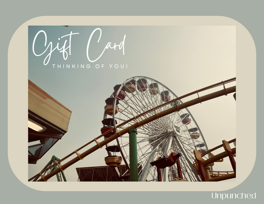 Card overlaying a rectangular background. Photo on the gift card of a ferris wheel. The top left corner of the photo card reads "Gift Card, Thinking of You!". In the bottom right corner the Unpunched logo is listed on the rectangle. Hues of taupe, soft grays with white words.