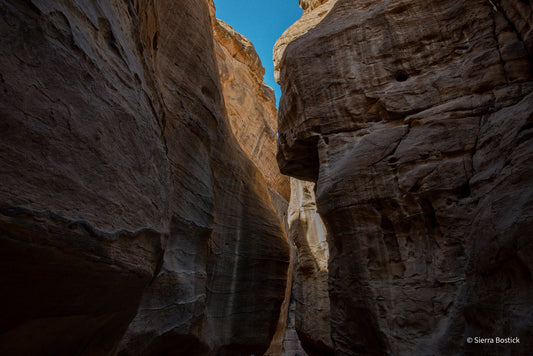 Upward view of the Al Siq Canyon in Jordan. Surrounded by striated red rock, that looks gold. At the top center of the picture there is a clear blue path of sky.